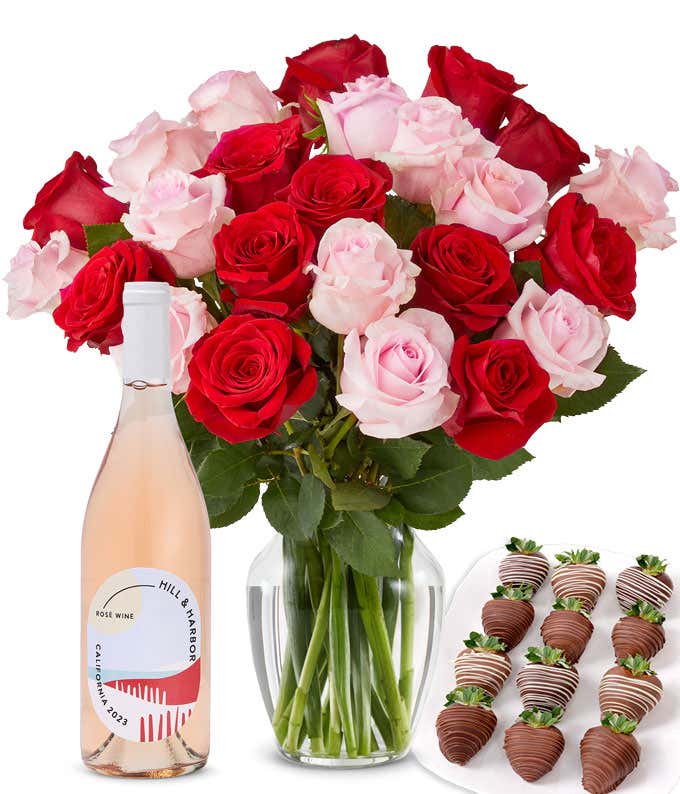 A mixed bouquet of 2 dozen red and blush roses in a clear vase is paired with a bottle of Hill & Harbor Rosé and 12 chocolate-covered strawberries.