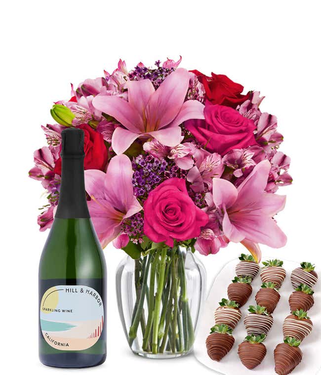 A mixed bouquet of pink and purple flowers in a clear glass vase is displayed with a bottle Hill &amp; Harbor Sparkling Wine and 12 chocolate-covered strawberries.