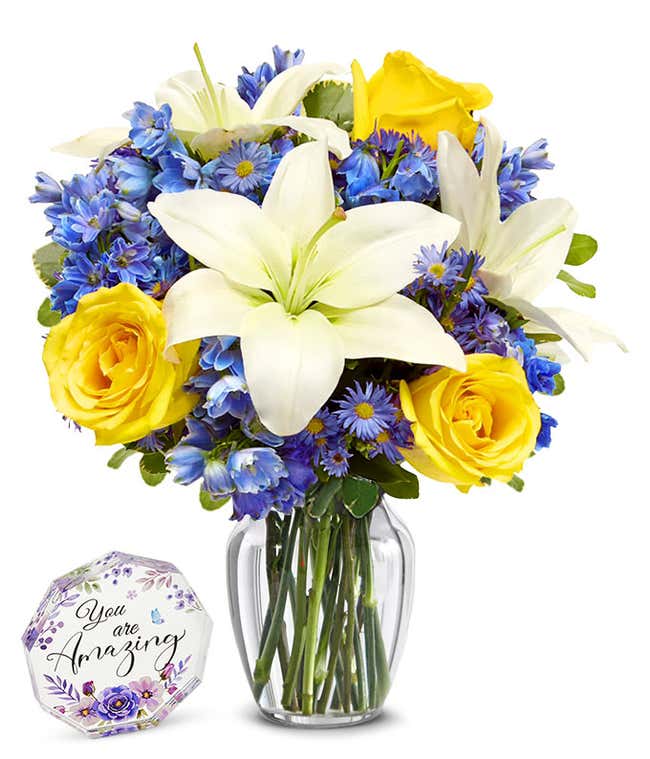 An elegant floral arrangement featuring white Asiatic lilies, yellow roses, blue delphinium, and purple Monte Casino, optionally arranged in a glass vase. This vibrant mix offers a stunning and colorful display.