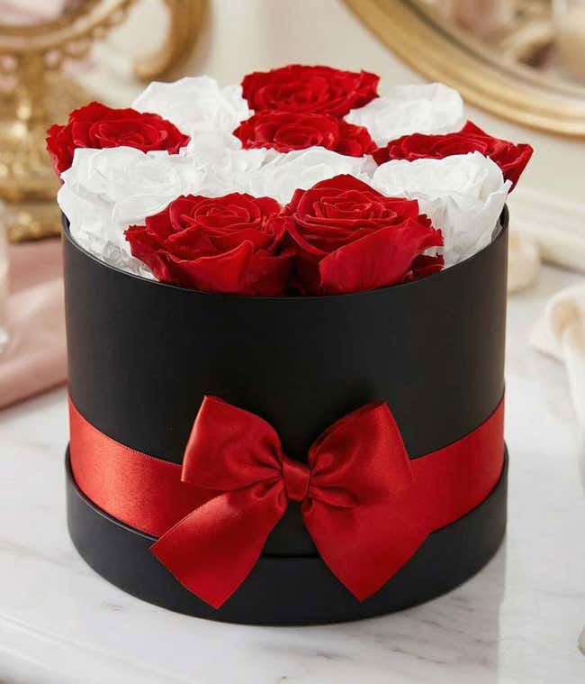 Elegant arrangement of red and white roses in a black round box, adorned with a red satin ribbon and bow, creating a sophisticated and romantic floral gift.