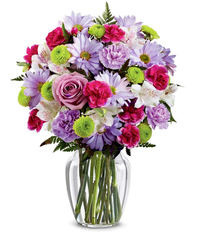A bouquet featuring lavender daisies, lavender roses, hot pink mini carnations, lavender carnations, white alstroemeria, and green button poms, with an optional vase.