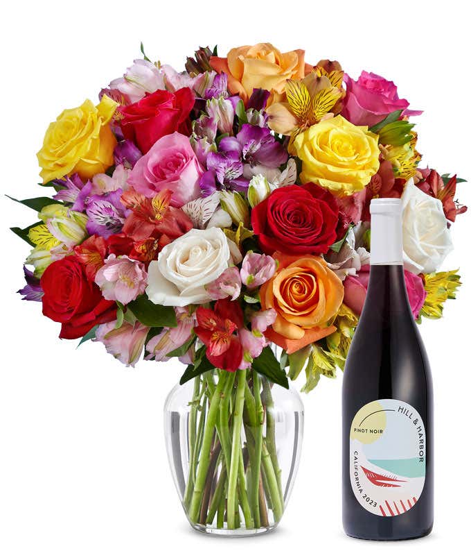 A mix bouquet of roses and alstroemeria fills a clear glass vase and is paired with a bottle of Hill & Harbor California Pinot Noir.