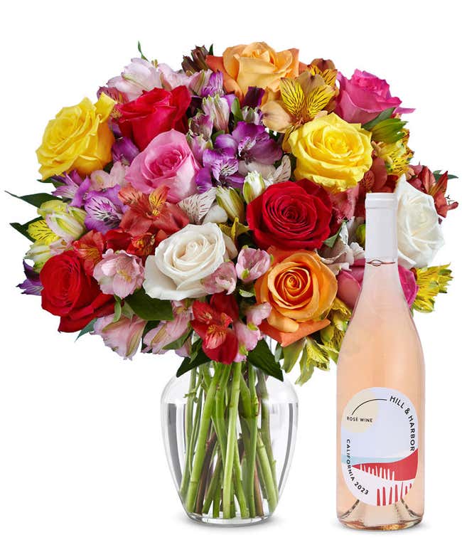 A mix bouquet of roses and alstroemeria fills a clear glass vase and is paired with a bottle of Hill &amp; Harbor California Pinot Noir.
