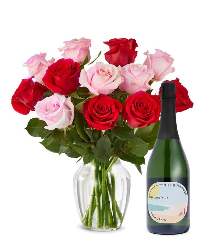 A mix bouquet of one dozen red and blush roses fills a clear glass vase and is paired with a bottle of Hill &amp; Harbor California Sparkling Wine.
