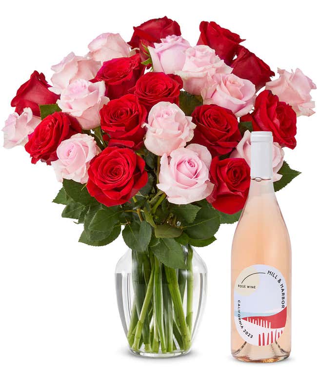 A mix bouquet of two dozen red and blush roses fills a clear glass vase and is paired with a bottle of Hill &amp; Harbor California Ros&eacute;.