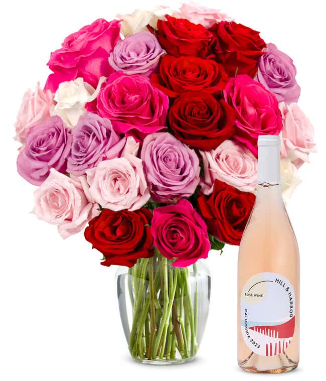 Two dozen pink, purple and red roses arranged in a clear glass vase sits beside a bottle of Hill &amp; Harbor California Ros&eacute;.