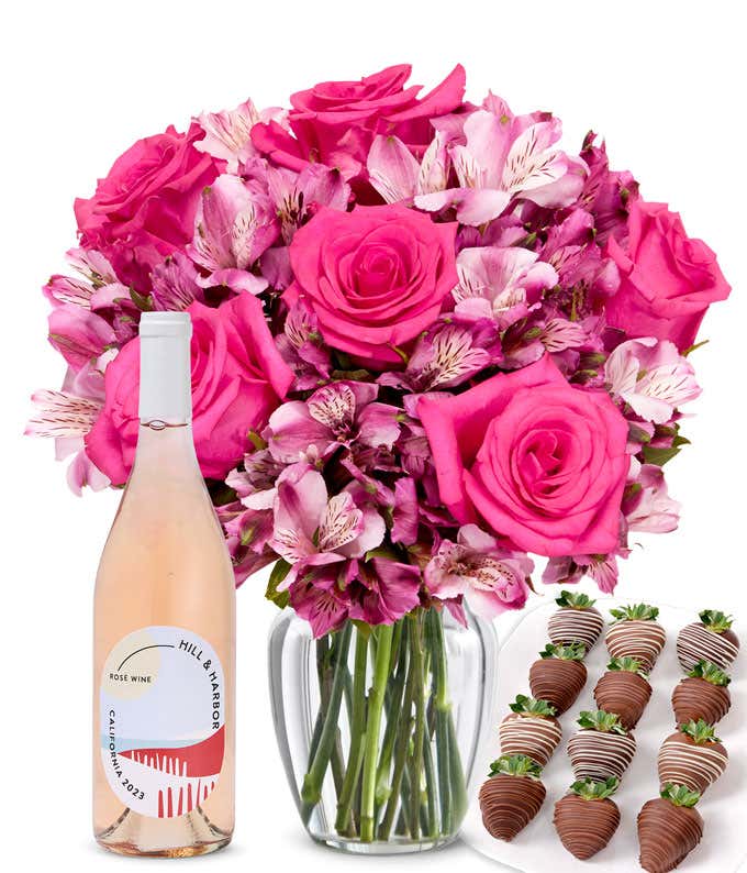 A clear glass vase filled with a pink roses & alstroemeria paired with a bottle of rosé wine and 12 chocolate-covered strawberries.