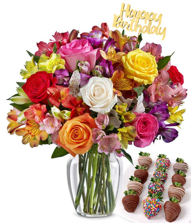 Flower arrangement with mixed roses and multicolor alstroemeria in a clear glass vase, accented with a gold Happy Birthday pick and paired with chocolate-covered strawberries in festive drizzle and rainbow sprinkle designs.