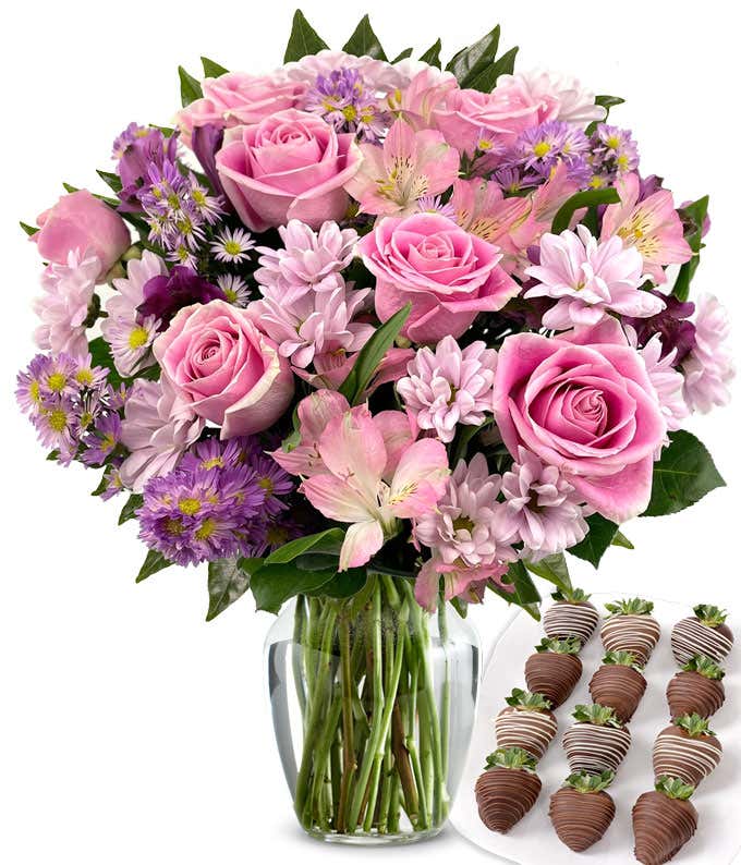  Deluxe bouquet of pink roses, lavender cushion poms, pink and purple alstroemeria, and purple asters in a clear glass vase, paired with swizzled chocolate-covered strawberries.