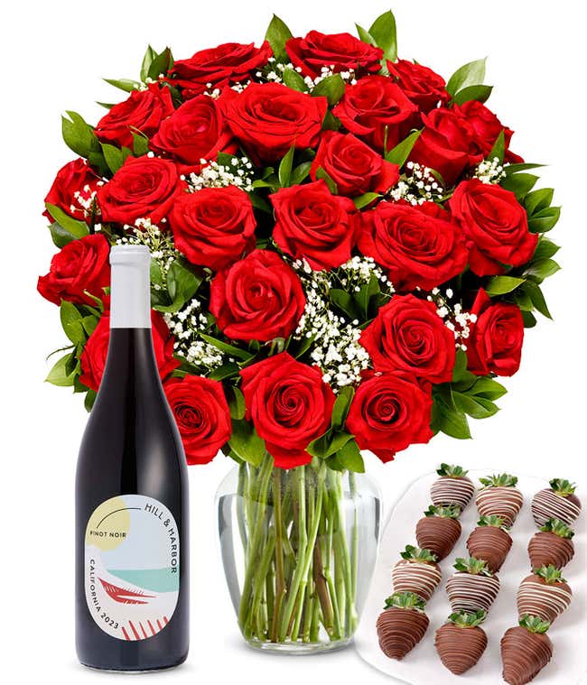 A bouquet of 2 dozen red roses in a clear glass vase is displayed beside a bottle of Hill &amp; Harbor Pinot Noir and an arrangement of 12 chocolate-covered strawberries.