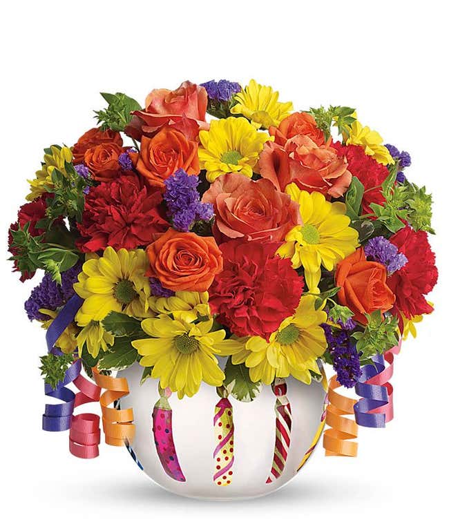 A festive arrangement featuring orange spray roses, red mini carnations, and yellow daisy spray mums, presented in a birthday cake inspired vase. This lively mix offers a fun and celebratory display.