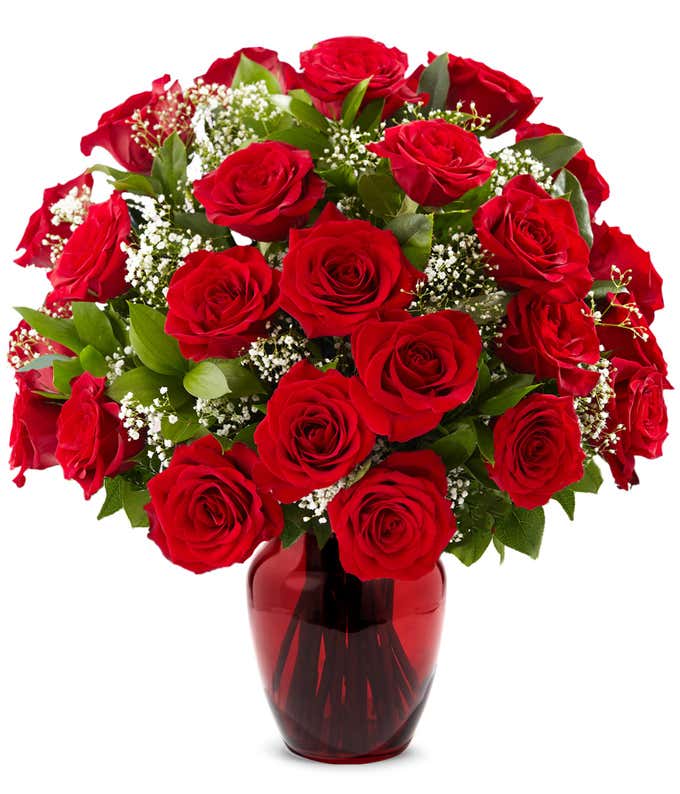 Red rose bouquet with baby's breath and greenery arranged in a deep red glass vase.