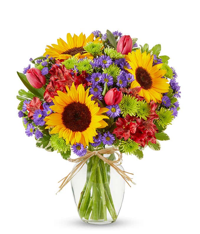 Sunflowers and pastel flowers in a clear glass vase with raffia tie