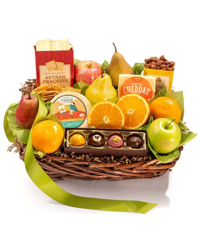 A basket filled with fresh fruits, crackers, cheese crisps, almonds, honey mustard, and assorted caramels, adorned with a green ribbon. 