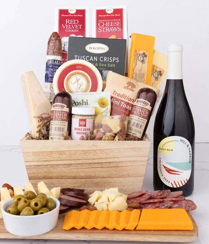 Wooden basket filled with 4 cheeses, 3 sausages, crackers, cookies, nuts, mustard, olives and crisps alongside a bottle of Hill & Harbor Pinot Noir.