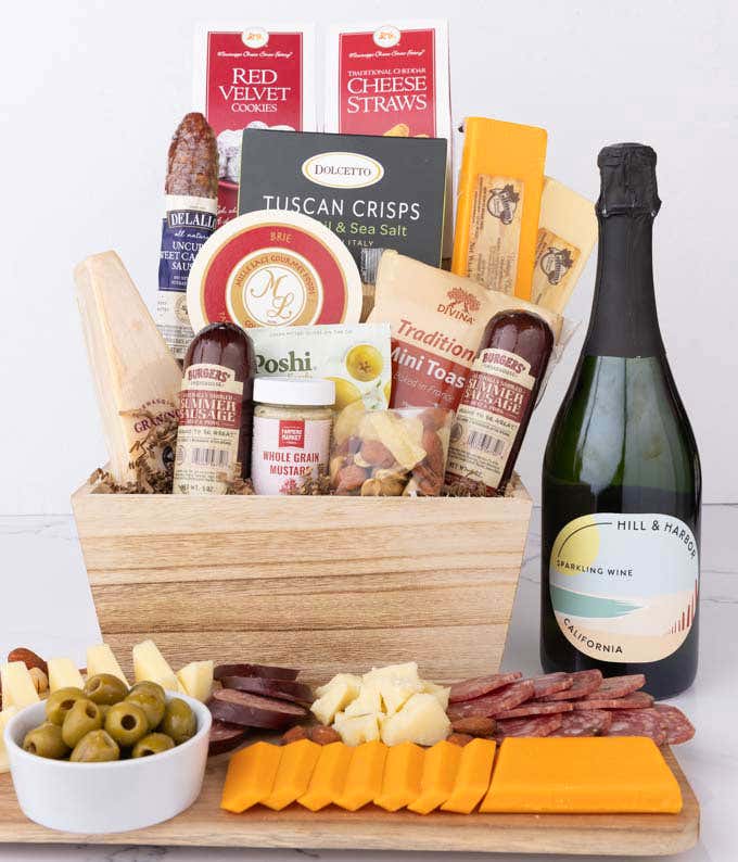 Wooden basket filled with 4 cheeses, 3 sausages, crackers, cookies, nuts, mustard, olives and crisps alongside a bottle of Hill & Harbor Sparkling Wine.