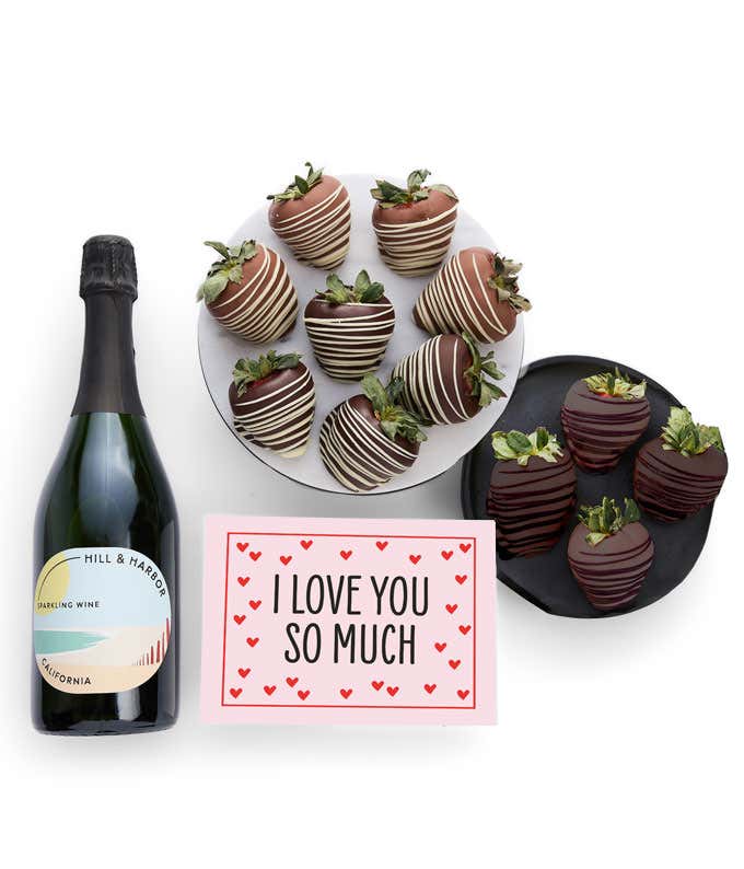 A bottle of Hill & Harbor California Sparkling Wine is displayed beside 12 assorted chocolate-covered strawberries, drizzled in milk and dark chocolate and a card saying, 'I Love You'.