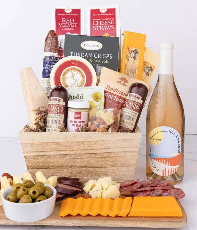 Wooden basket filled with 4 cheeses, 3 sausages, crackers, cookies, nuts, mustard, olives and crisps alongside a bottle of Hill & Harbor Rosé wine.