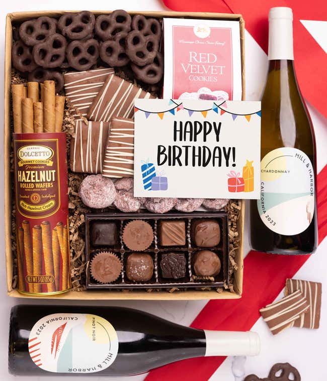 A gift box with chocolate pretzels, chocolate graham crackers, red velvet cookies, hazelnut wafer rolls, an 8 piece box of chocolates, 2 bottles of wine and a Birthday message card.