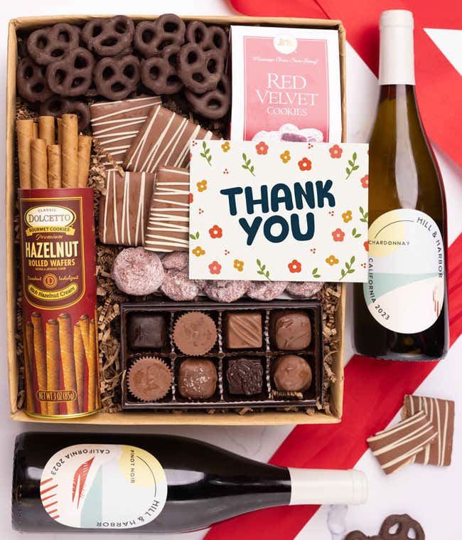 A gift box with chocolate pretzels, chocolate graham crackers, red velvet cookies, hazelnut wafer rolls, an 8 piece box of chocolates, 2 bottles of wine and a Thank You message card.