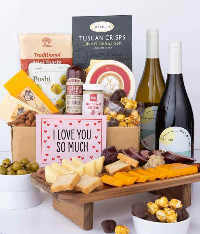 A luxurious gift box with a bottle of Hill & Harbor Pinot Noir, three cheeses, gourmet crackers, summer sausage, marinated olives, smoked almonds, stone-ground mustard, chocolate-covered, and a pink 'I Love You So Much' card