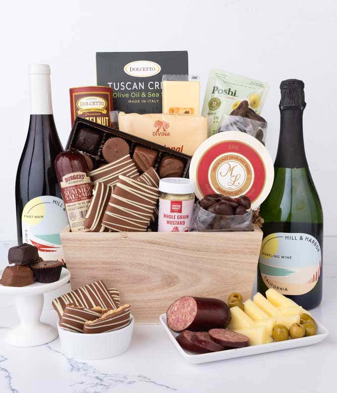 Wooden crate filled with gourmet snacks and two bottles of Hill & Harbor wine,  Sparkling Wine and Pinot Noir, alongside artisan summer sausage, creamy cheeses, assorted chocolates, striped chocolate-covered grahams, cookies, crisps, mustard, and olives.