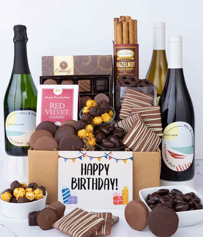A gift box overflowing with treats including an assortment of chocolate-covered items like oreoes, almonds graham crackers and pretzels along with red velvet cookies, hazelnut wafers, an 8 piece box of chocolates, 3 bottles of wine and a Birthday card.