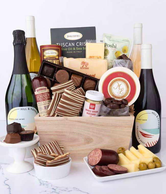 Wooden crate filled with gourmet food and 4 bottles of wine, including Chardonnay, Pinot Noir, Sparkling Wine, and Ros&eacute;, alongside artisan summer sausage, creamy cheeses, assorted chocolates, striped chocolate grahams, cookies, crisps, mustard, and olives